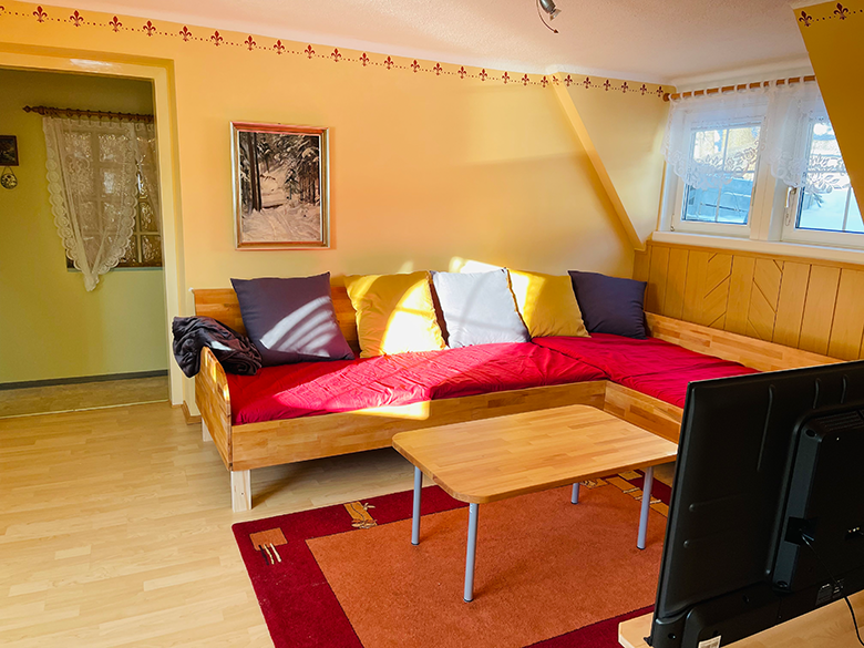 Wohnzimmer mit rotem Sofa, Holztisch und Fernseher.