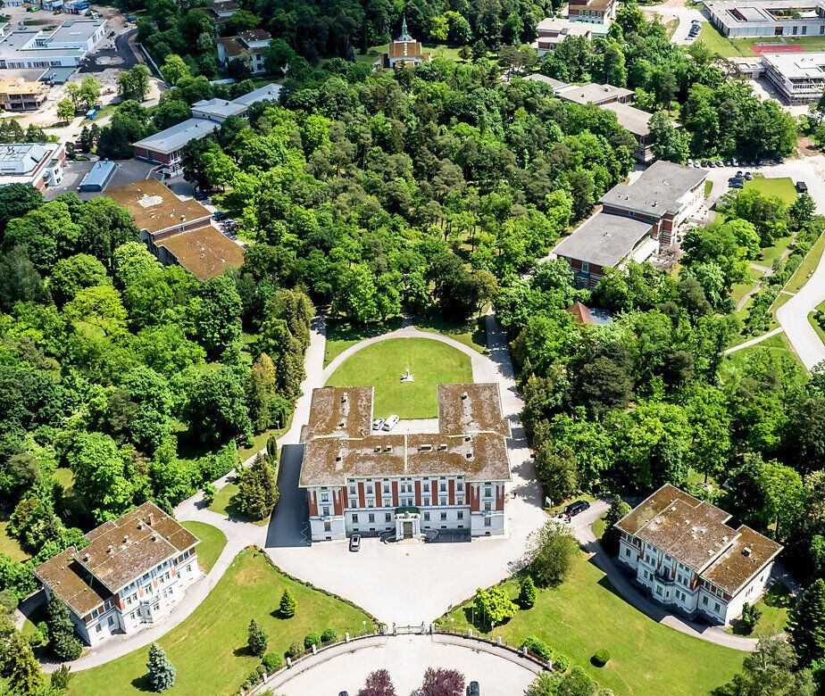 Luftaufnahme des weitläufigen Areals des Landesklinikums Mauer im Mostviertel mit historischen Gebäuden, Parkanlagen und dichtem Baumbestand, Austragungsort der Niederösterreichischen Landesausstellung 2026.