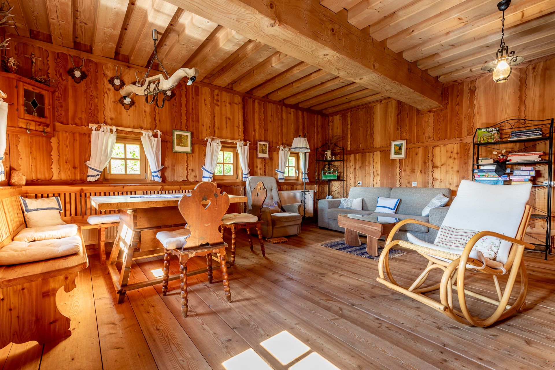 Essbereich mit Holzmöbeln, Schaukelstuhl und Sofa in einem Raum mit Holzvertäfelung.