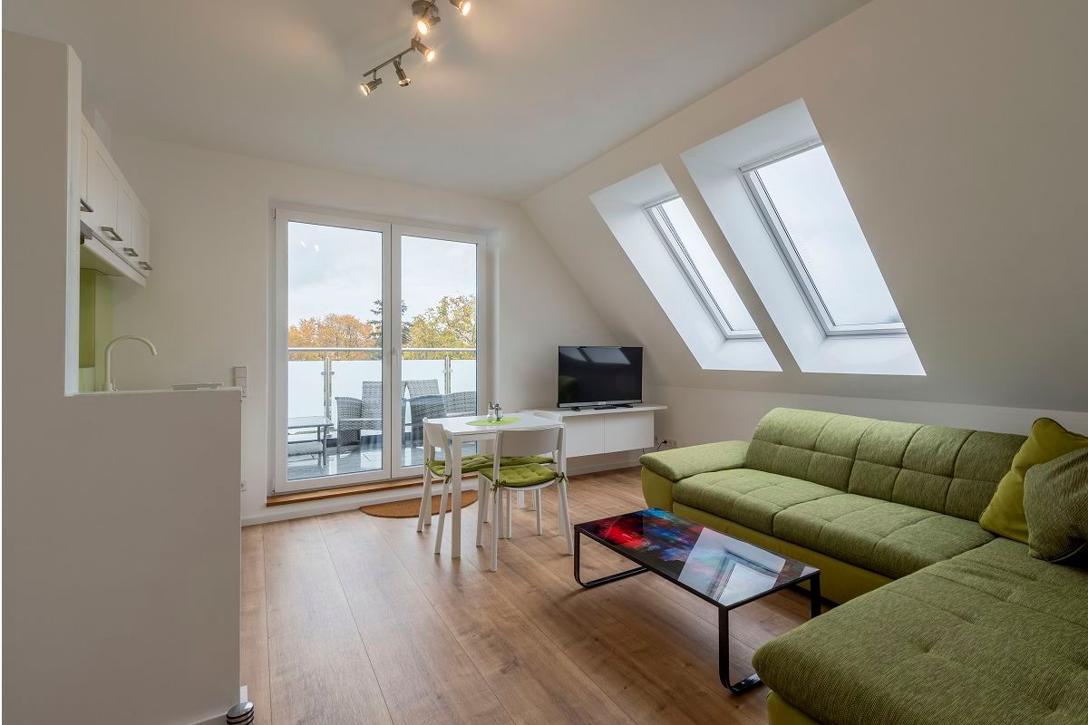 Modernes Wohnzimmer mit grüner Couch, Glastisch, TV und Balkonzugang.