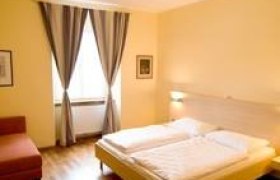 Ein gem&uuml;tliches Doppelzimmer mit einem gro&szlig;en Bett, Holzboden, einem Sessel und einem Fenster mit Vorh&auml;ngen.