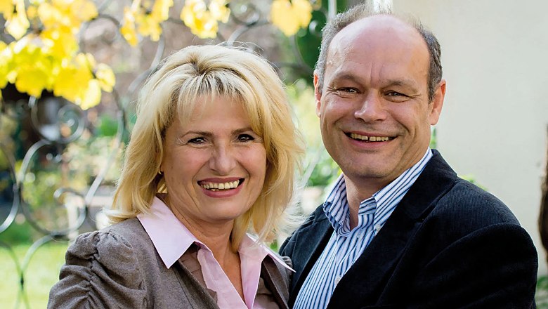 Ein lächelndes Paar steht draußen vor einem Hintergrund mit gelben Blättern.