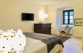 Gem&uuml;tliches Schlafzimmer mit Bett, antiker Kommode, Sessel und Wand-TV.