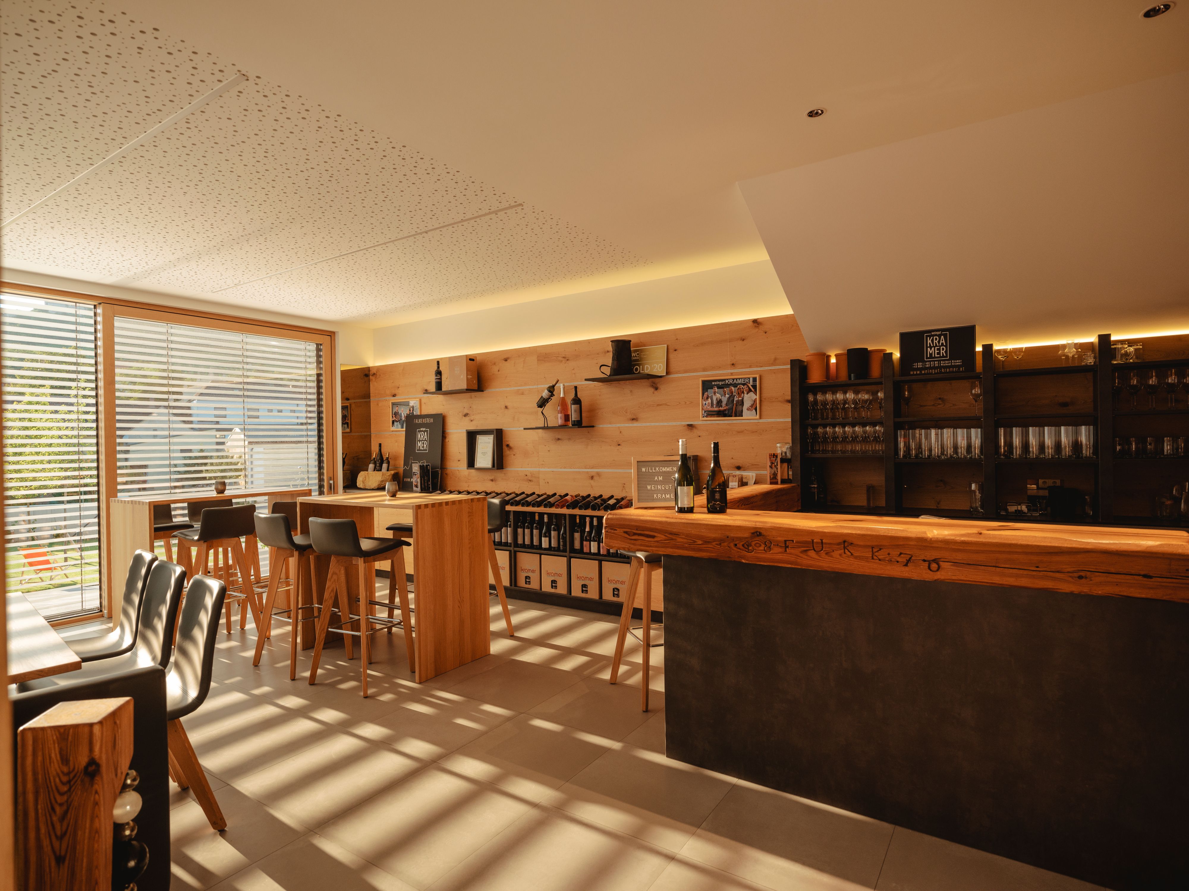 Innenansicht einer modernen Weinbar mit Holzmöbeln und großen Fenstern.