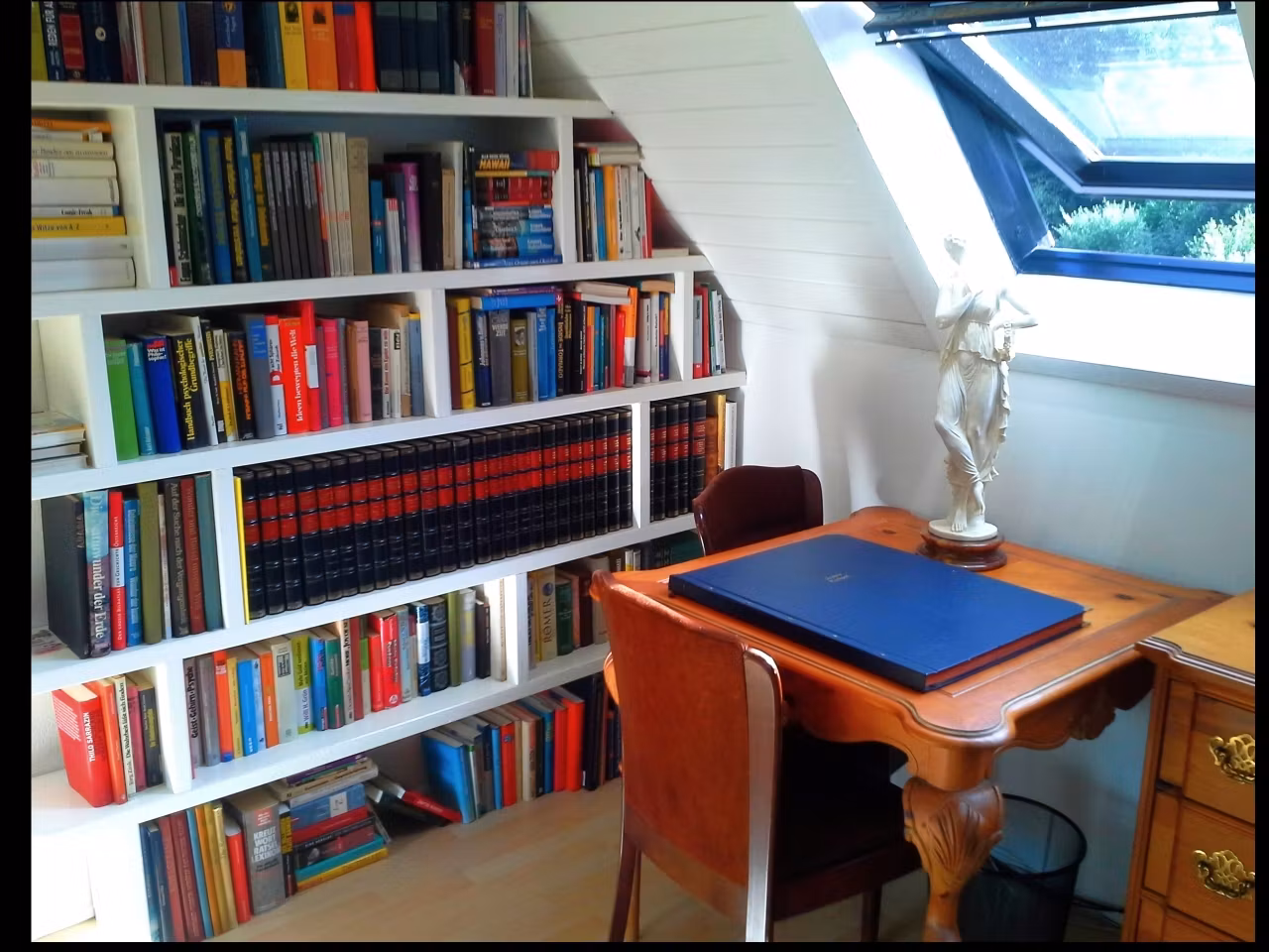 Ein gemütlicher Arbeitsbereich mit Bücherregal, Schreibtisch und Statue.