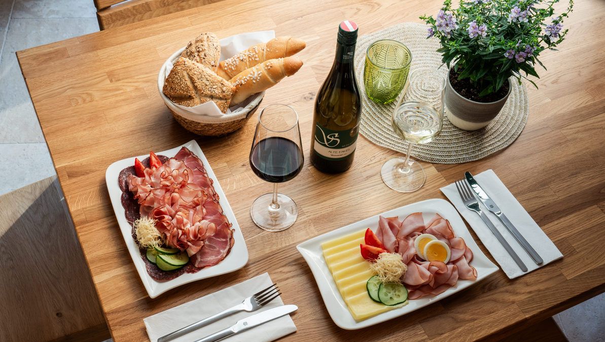 Ein Tisch mit regionalen Köstlichkeiten: Aufschnitt, Käse, Brot, Rot- und Weißwein.