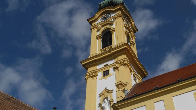 Gelber Kirchturm der Stadtpfarrkirche Stockerau vor blauem Himmel.