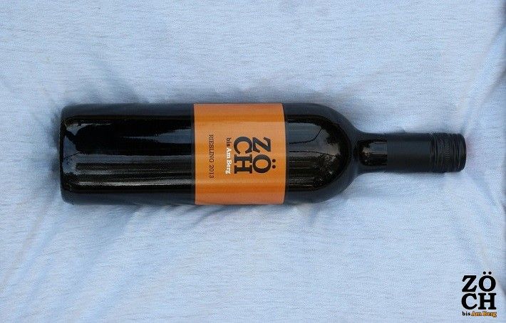 Eine Weinflasche mit orangefarbenem Etikett der Marke Zöch auf einem hellen Hintergrund.