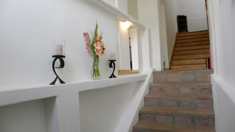 Innenansicht eines Treppenaufgangs mit Kerzenhaltern und Blumen auf einem Sims.