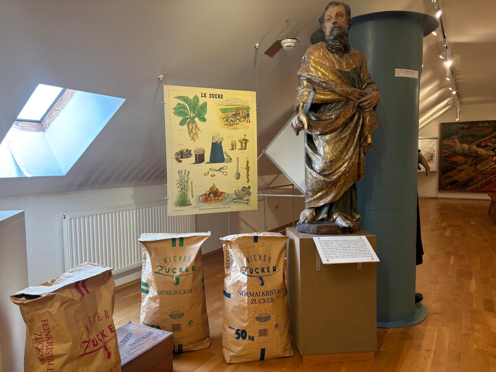 Ausstellung im Zuckermuseum mit Statue, Zuckersäcken und Poster.