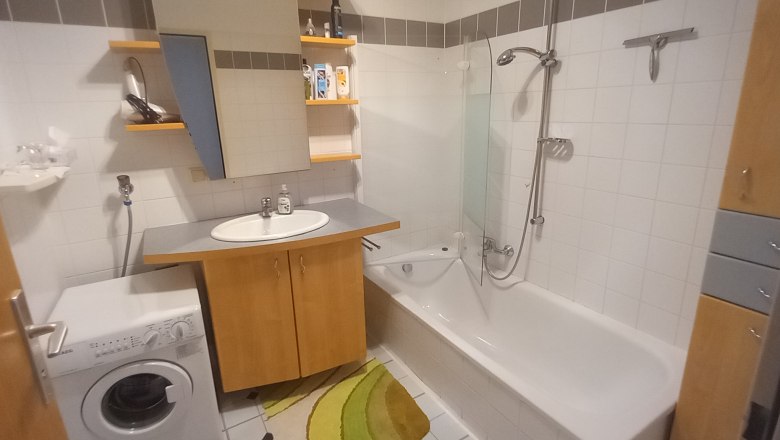 Modernes Badezimmer mit Waschmaschine, Waschbecken, Badewanne und Regalen.