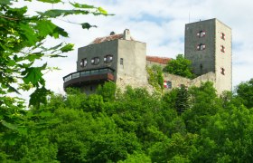 Burg Greifenstein auf einem bewaldeten Hügel mit blauem Himmel im Hintergrund.