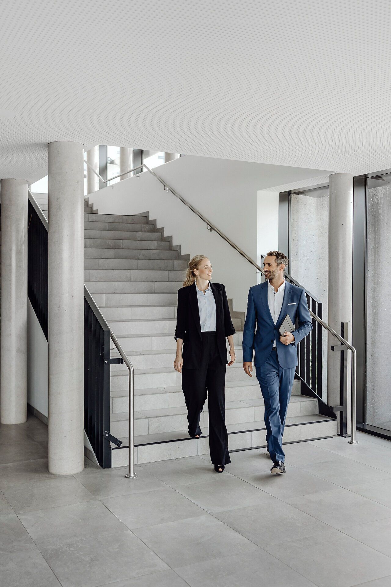 In einem modernen Ambiente schlendern zwei Geschäftspartner entspannt die Treppe hinunter. Ihre freundlichen Gesichter spiegeln die positive Atmosphäre wider, die in dieser inspirierenden Umgebung herrscht. Die hellen, offenen Räume laden dazu ein, kreative Ideen auszutauschen und neue Projekte zu entwickeln.