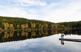 Die sanften H&uuml;gel spiegeln sich im ruhigen Wasser des Schlesinger Teichs, w&auml;hrend die bunten Bl&auml;tter der B&auml;ume den Herbst in voller Pracht zeigen. Ein romantischer Moment f&uuml;r Paare, die die friedliche Natur und die frische Luft genie&szlig;en m&ouml;chten.