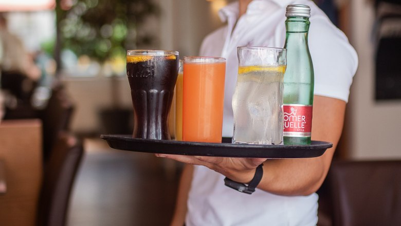 Eine l&auml;chelnde Kellnerin in einem Restaurant tr&auml;gt ein Tablett mit verschiedenen Getr&auml;nken.