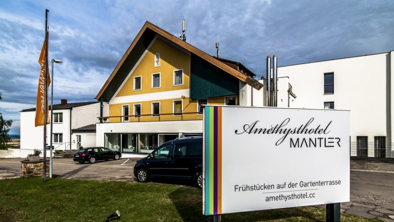 Amethysthotel Mantler, © Imre Antal Außenansicht des Amethysthotels Mantler mit Parkplatz und Schild.