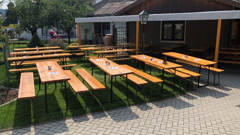 Holzbänke und Tische in einem Heurigengarten mit Sonnenschutz.