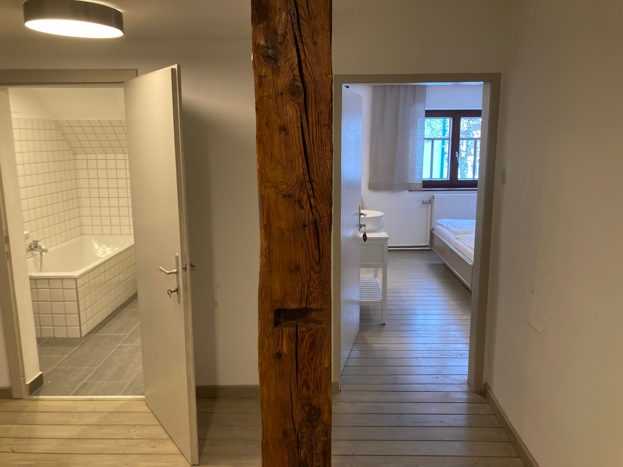 Ein Badezimmer und ein Schlafzimmer mit Holzboden, getrennt durch eine Holzbalkenwand.