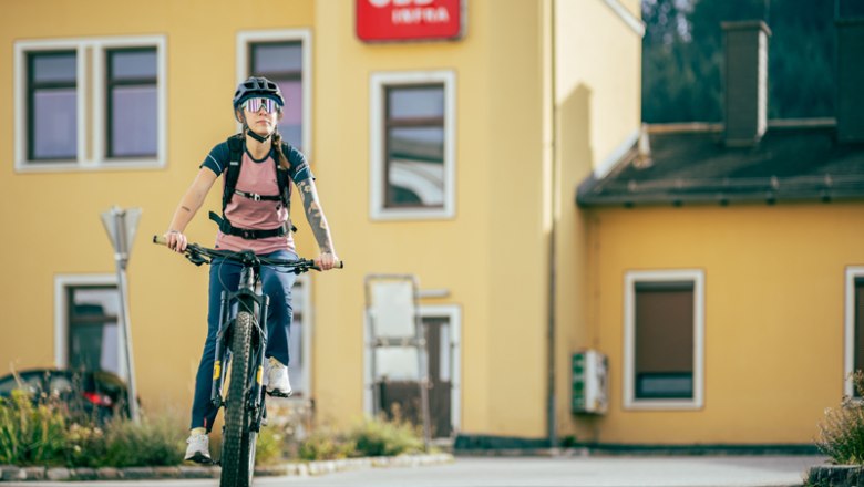 Person auf Fahrrad vor gelbem Geb&auml;ude mit &Ouml;BB-Logo.