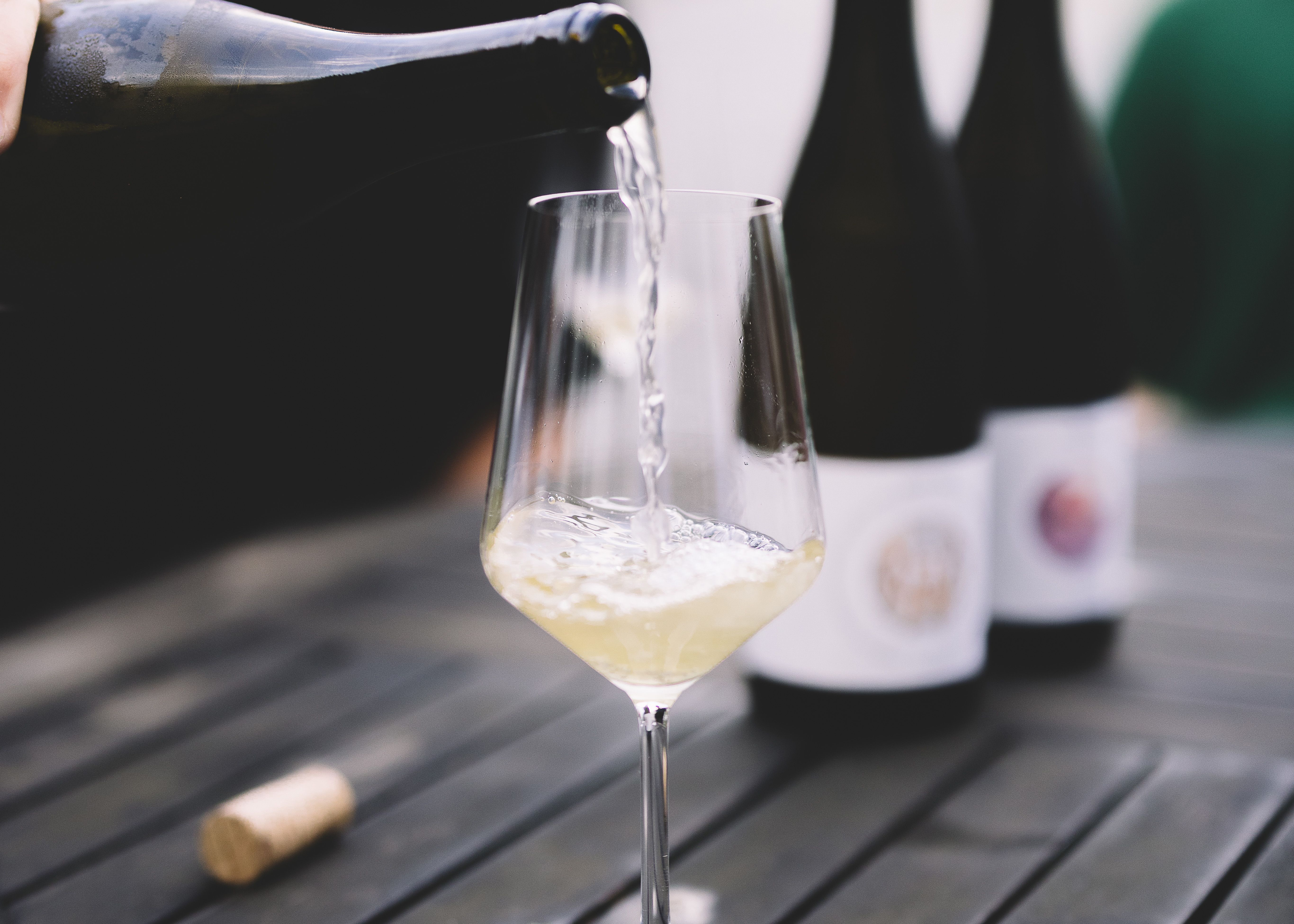 Ein Glas Weißwein wird auf einem Tisch eingeschenkt, mit zwei Weinflaschen im Hintergrund.