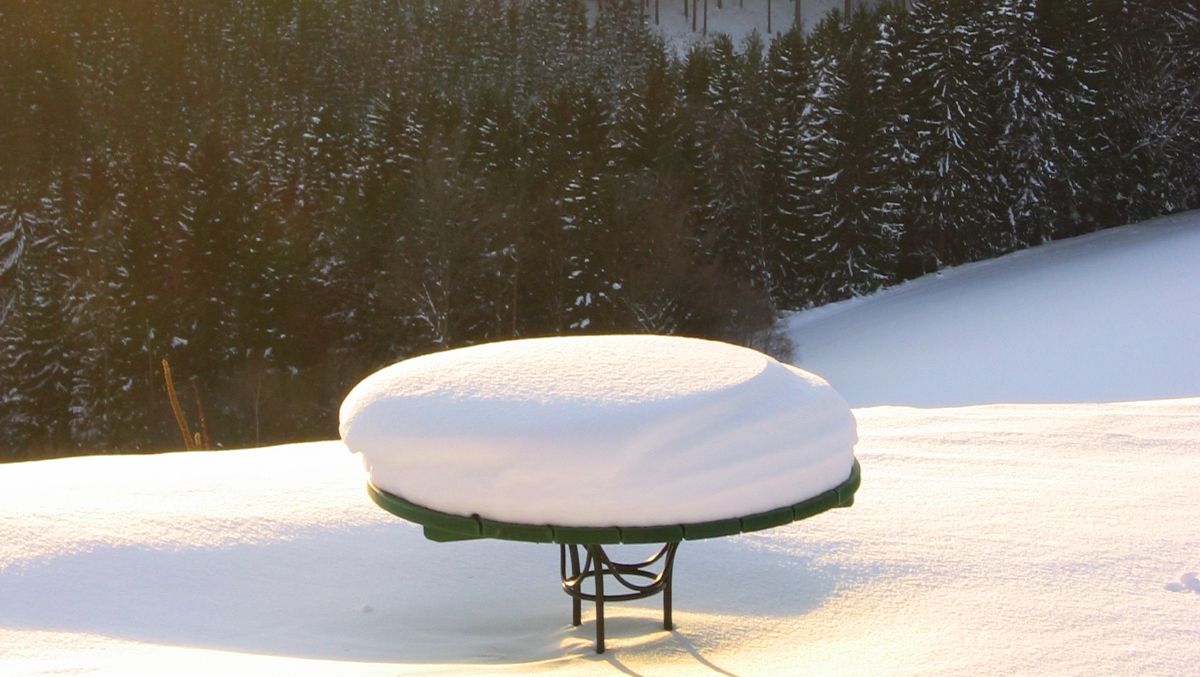 Schneebedeckter Tisch in winterlicher Landschaft mit Wald im Hintergrund.