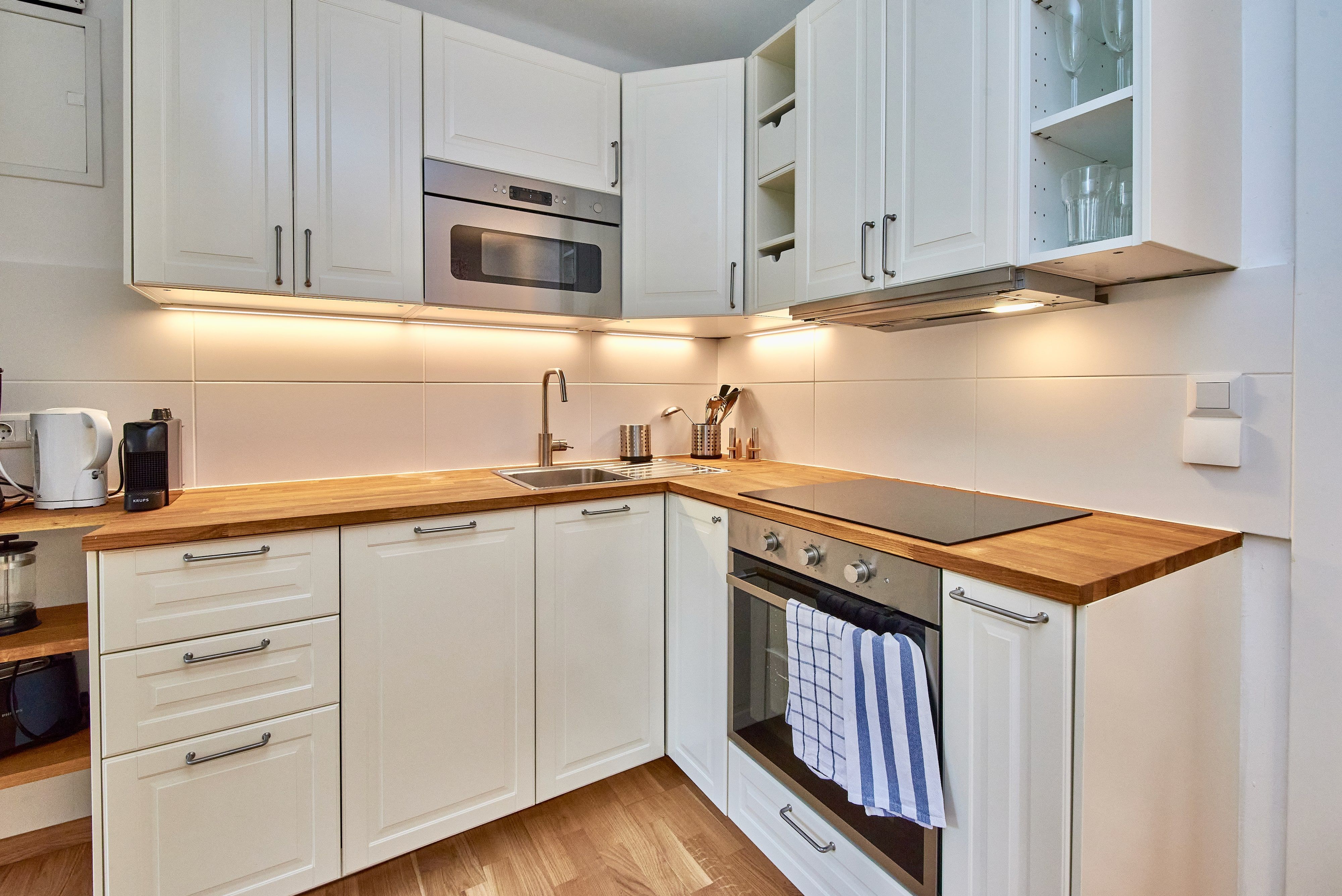 Moderne Küche mit weißen Schränken, Holzarbeitsplatten, Herd und Spüle.