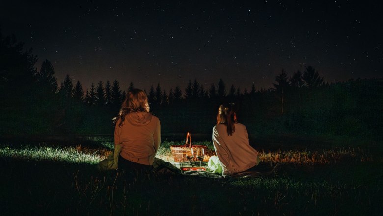 Zwei Personen sitzen nachts auf einer Wiese und schauen in den Sternenhimmel.