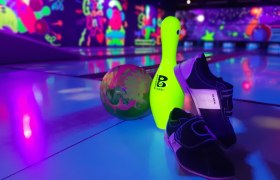 Bowlingkugel, Kegel und Schuhe auf einer Bowlingbahn mit neonfarbener Beleuchtung.