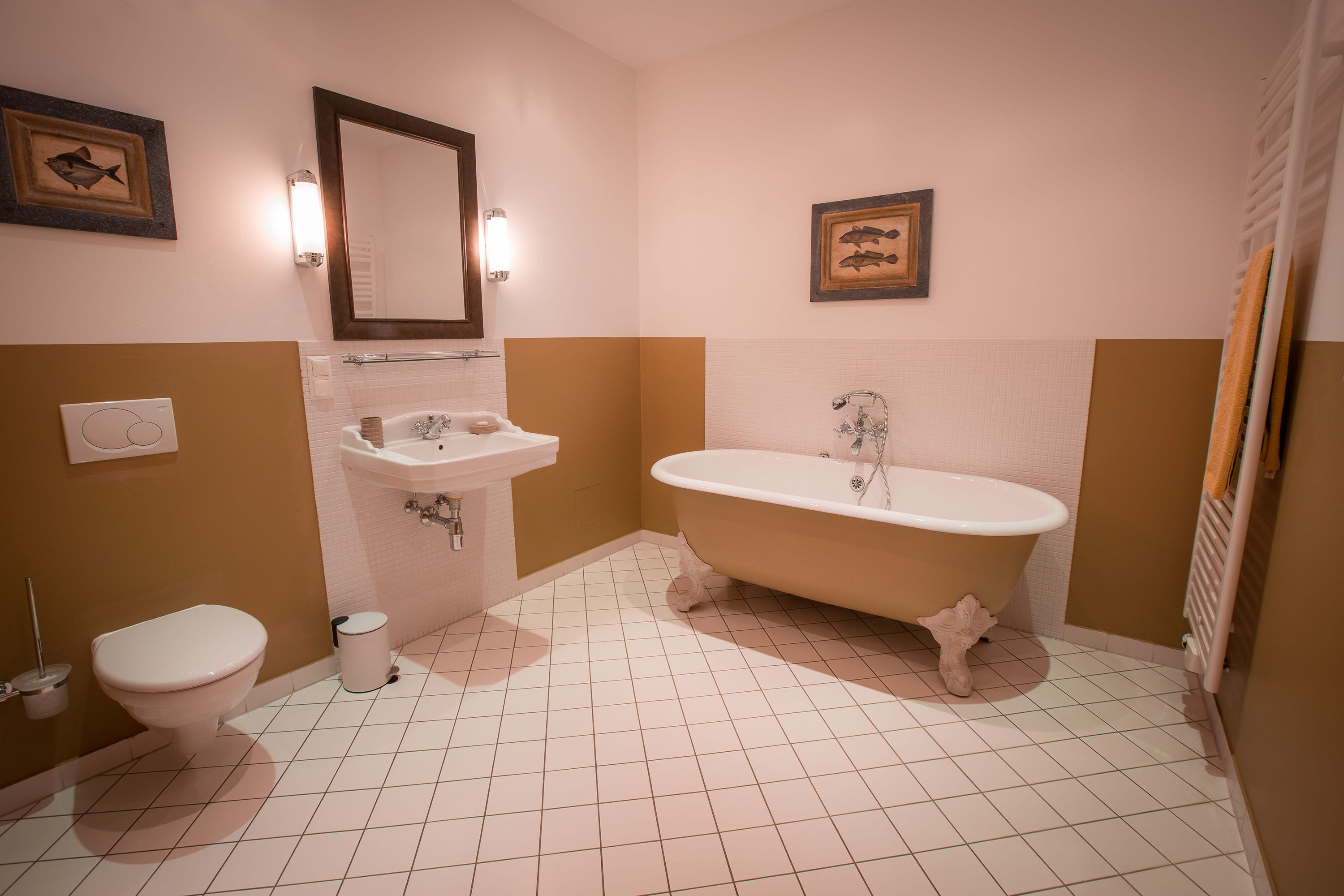 Elegantes Badezimmer mit freistehender Badewanne, Waschbecken, Spiegel und WC. Wände in Beige und Weiß, dekoriert mit Fischbildern.