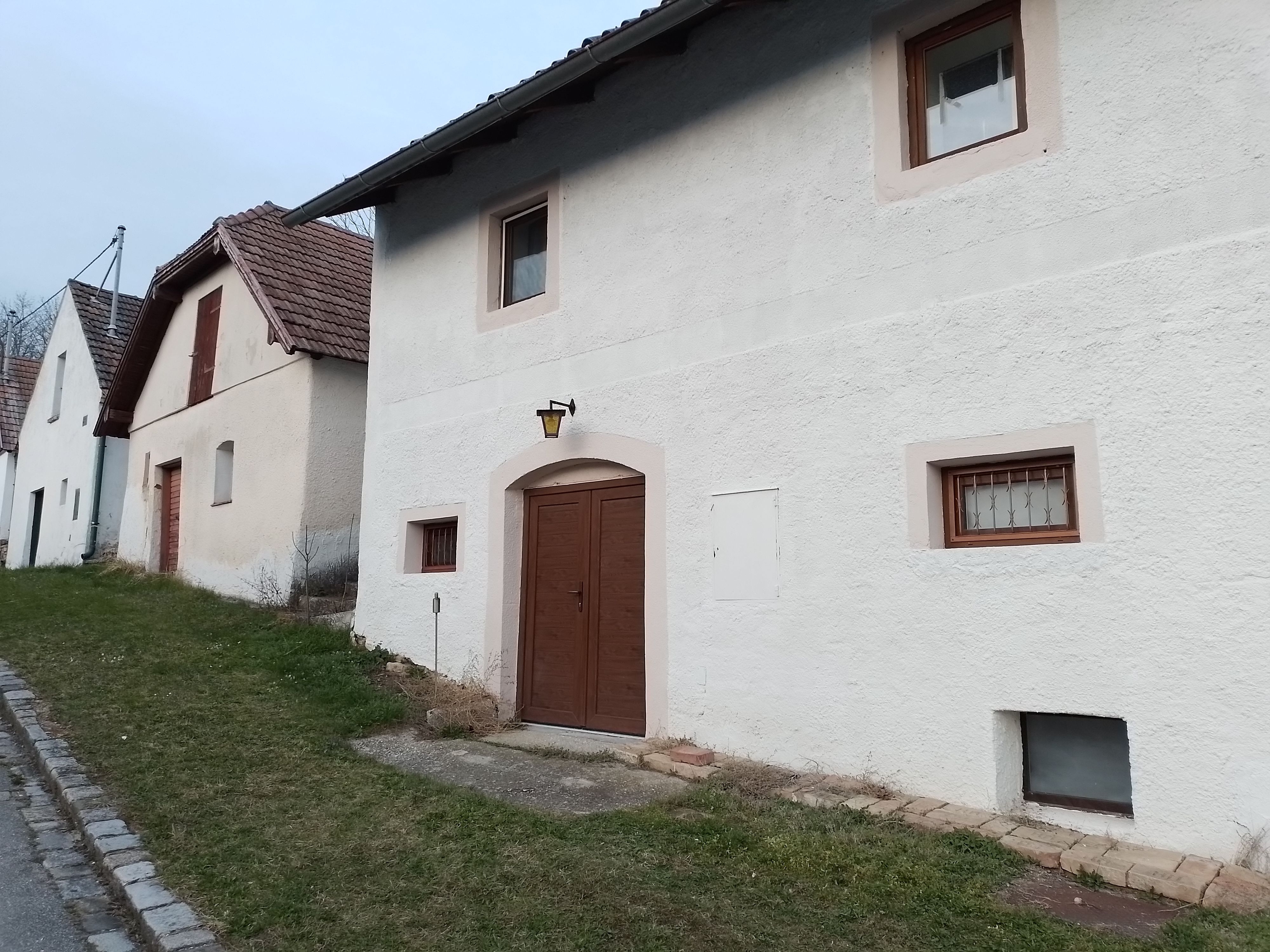 Reihen von weißen Häusern mit braunen Türen und Fenstern, entlang einer Straße mit Grasstreifen.