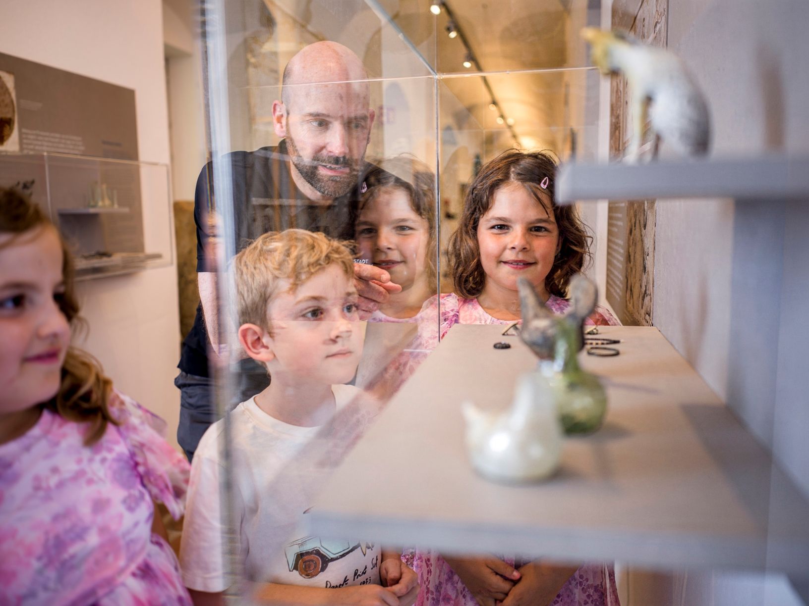 Erwachsener zeigt Kindern römischen Schmuck in Glasvitrine