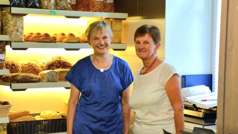 Zwei Frauen in einer B&auml;ckerei vor Regalen mit Brot und Geb&auml;ck.