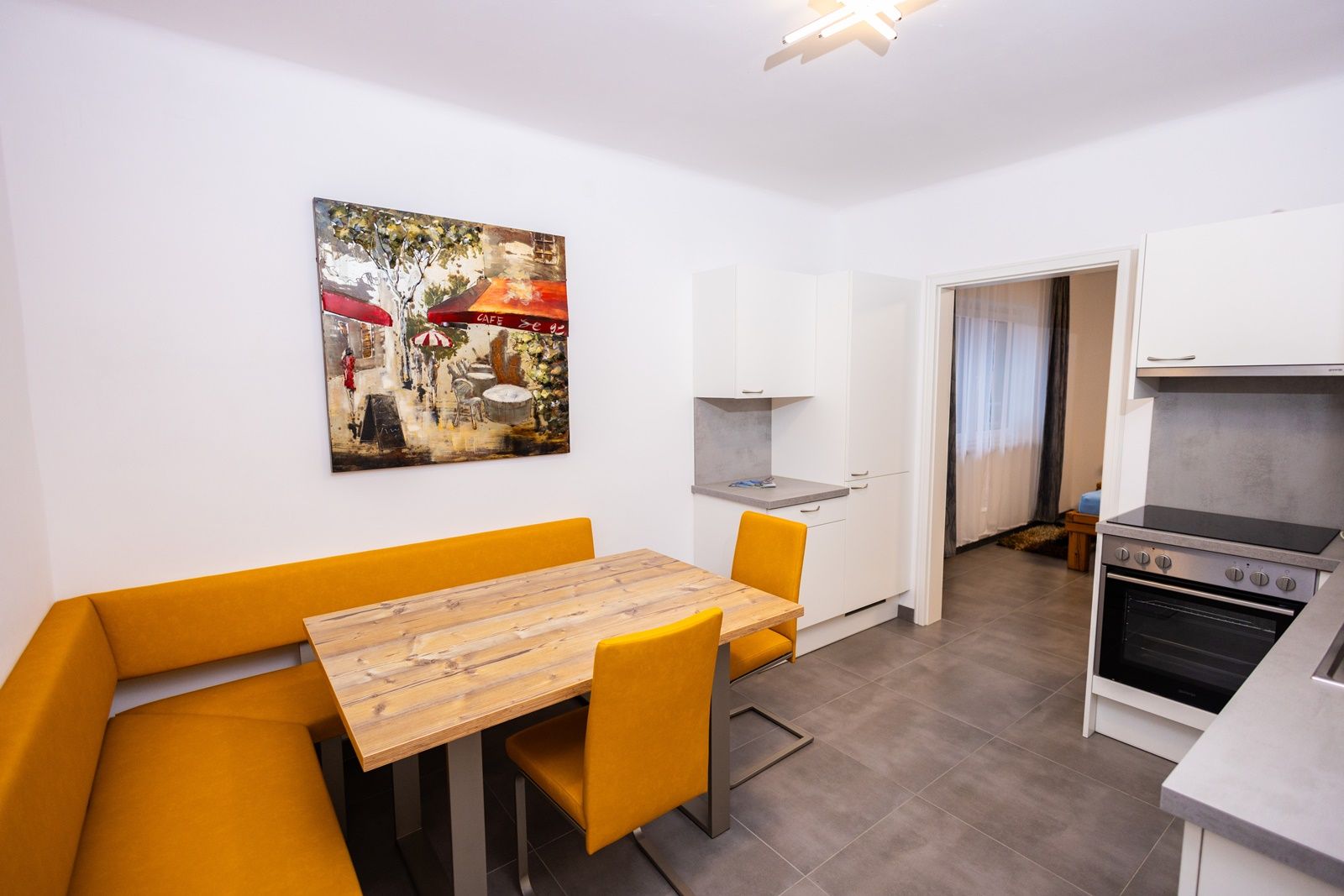 Moderne Küche mit gelber Eckbank, Holztisch und Kunstwerk an der Wand.