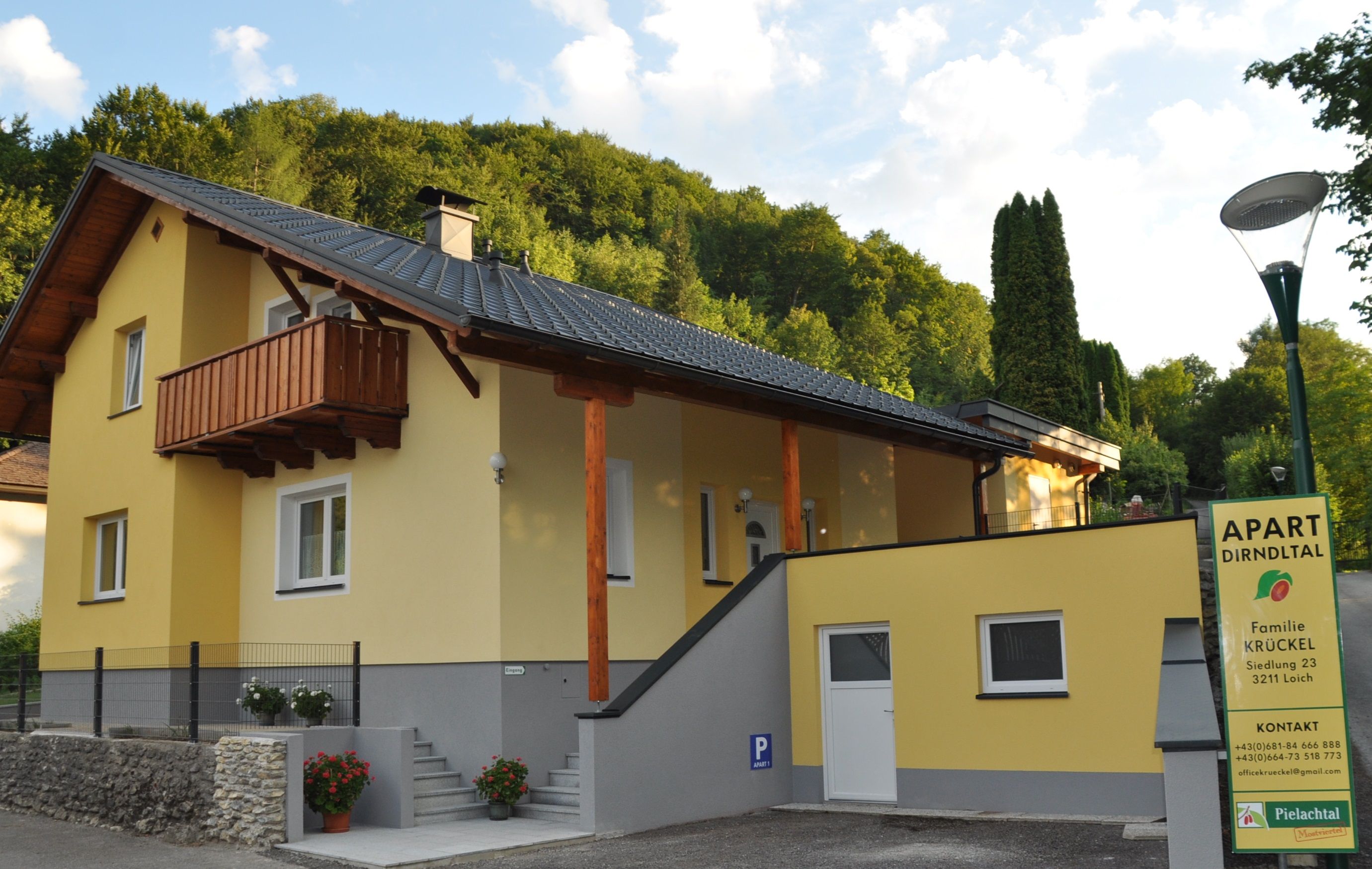 Gelbes Haus mit Balkon und Schild 'Apart Dirndltal' vor einem bewaldeten Hügel.