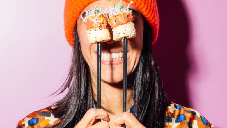 Person mit orangefarbener Mütze hält Sushi vor den Augen.