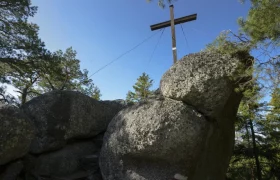 Große Felsen mit einem Holzkreuz auf einem bewaldeten Hügel.