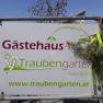 Schild mit der Aufschrift 'Gästehaus Traubengarten Winkler' und Website-Adresse, dekoriert mit Zweigen.