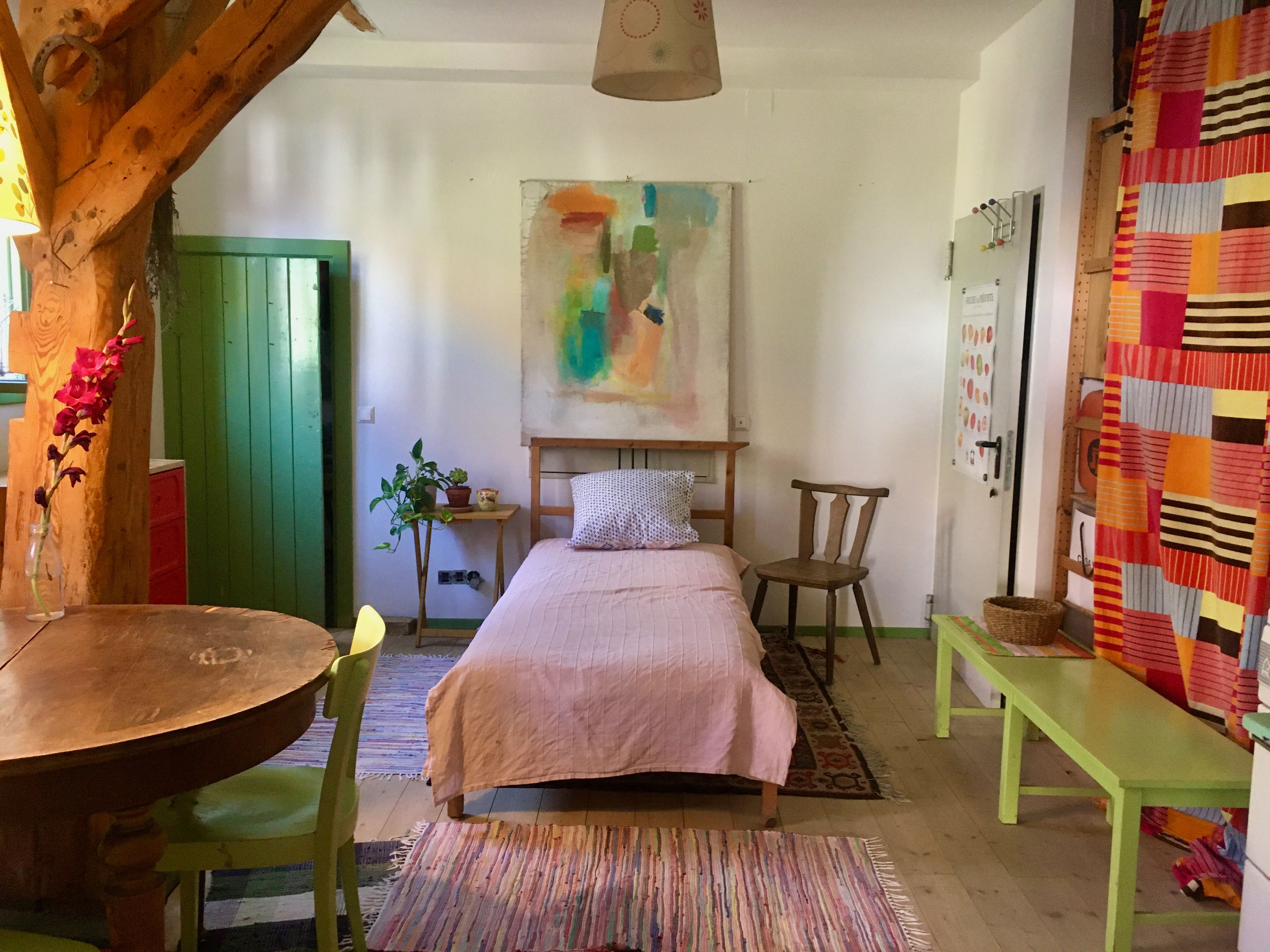 Einzelbett in einem Zimmer mit bunten Möbel und einem großem Gemälde über dem Bett.