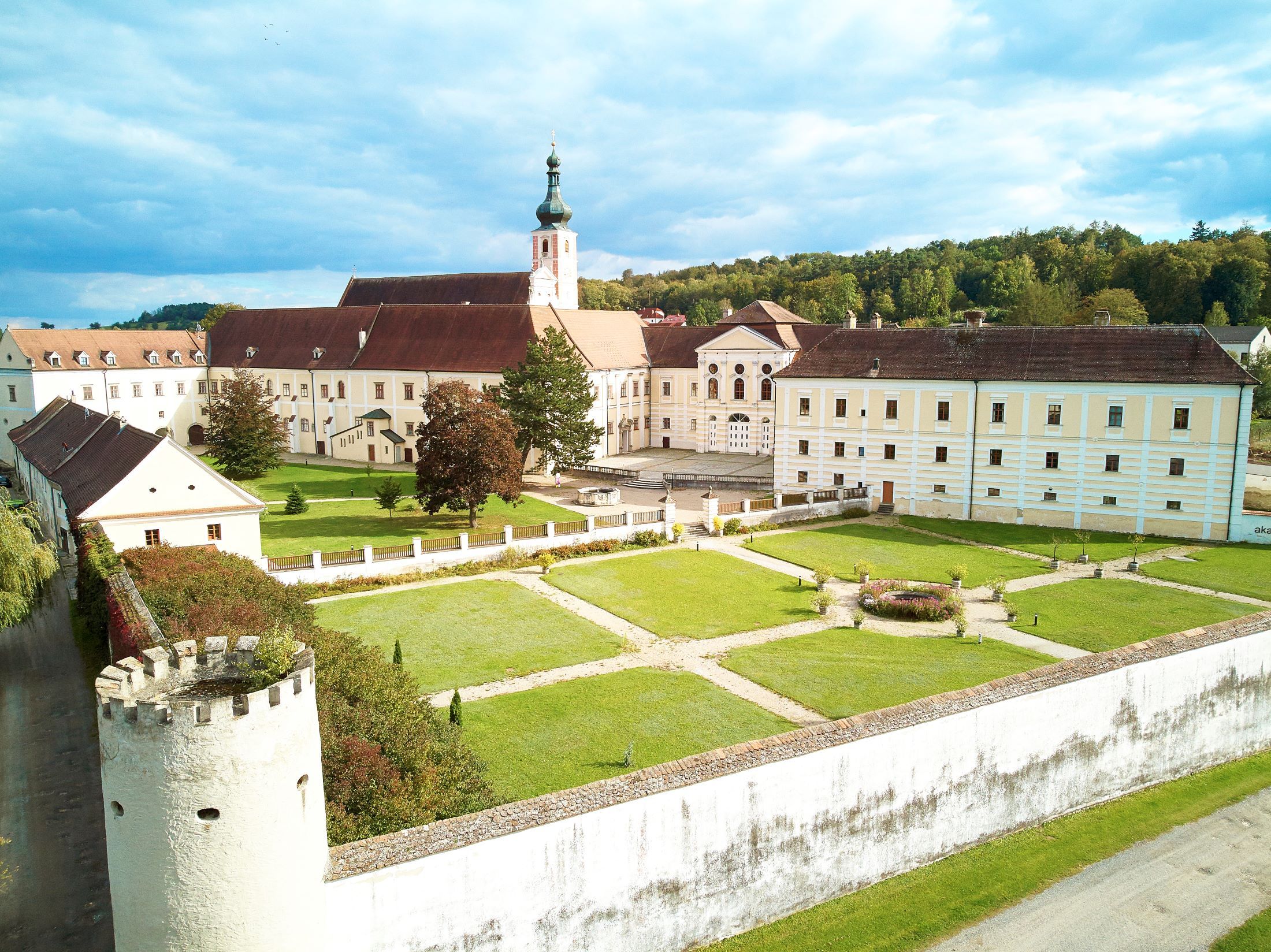 Luftaufnahme eines Klosters mit Garten und Turm, umgeben von Bäumen.