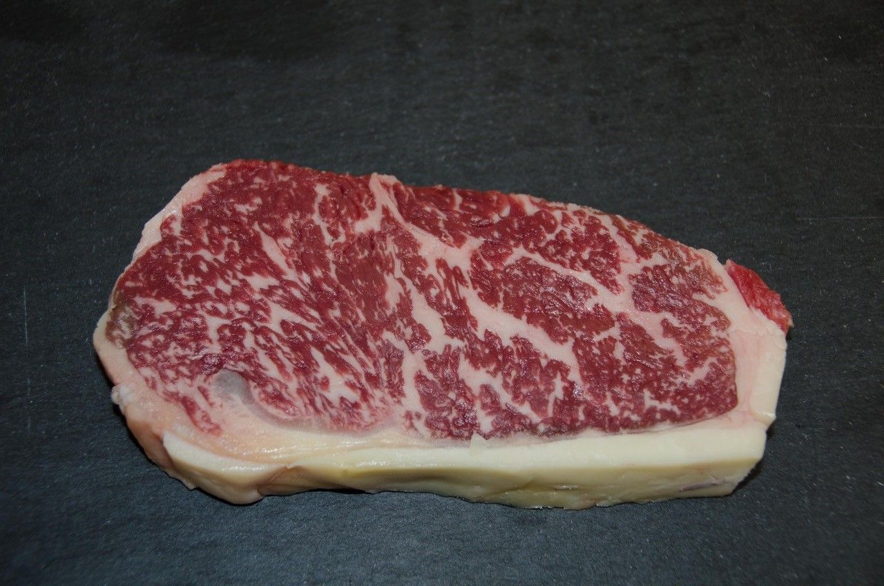 Ein Stück Wagyu-Rindfleisch mit starker Marmorierung auf schwarzem Hintergrund.
