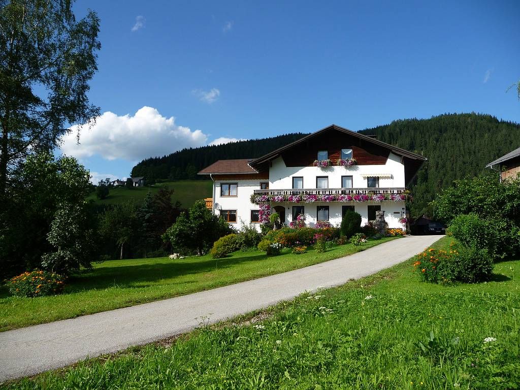 Ein Bauernhof mit Blumen geschmücktem Haus in einer grünen Landschaft unter blauem Himmel.