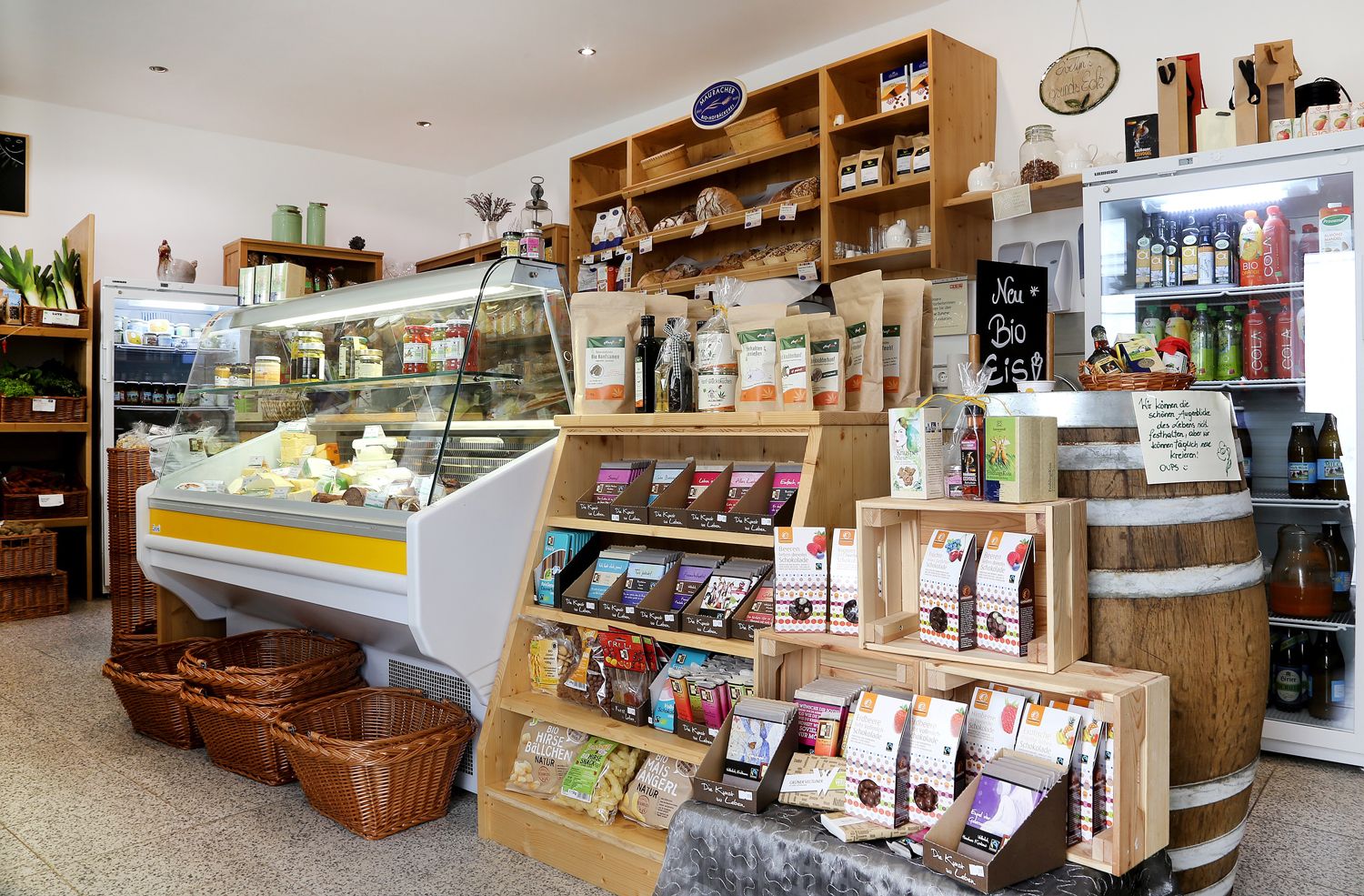 Innenansicht eines kleinen Ladens mit Regalen voller Bio-Produkte und einer Kühltheke mit Käse.