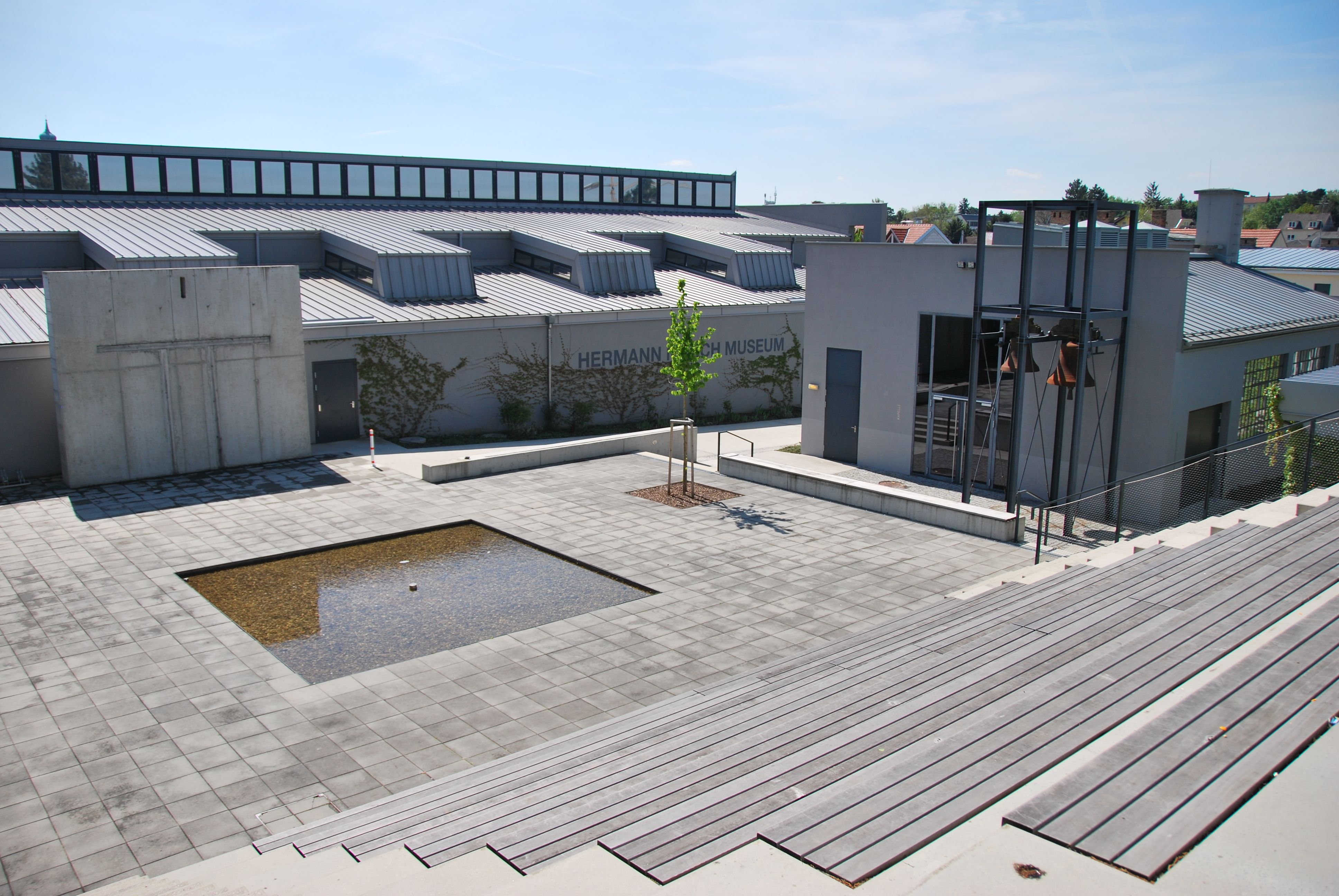 Außenansicht des Hermann Nitsch Museums mit modernem Design und einem kleinen Wasserbecken auf der Piazza.