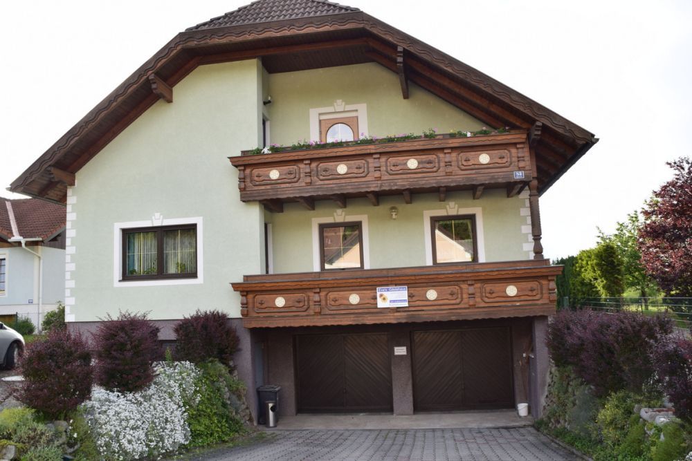 Ein zweistöckiges Haus mit grüner Fassade und Holzbalkonen, umgeben von gepflegten Gärten.