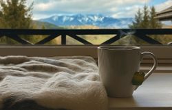 Kuscheldecke und Teetasse stehen am Fenster mit Aussicht auf die Berge