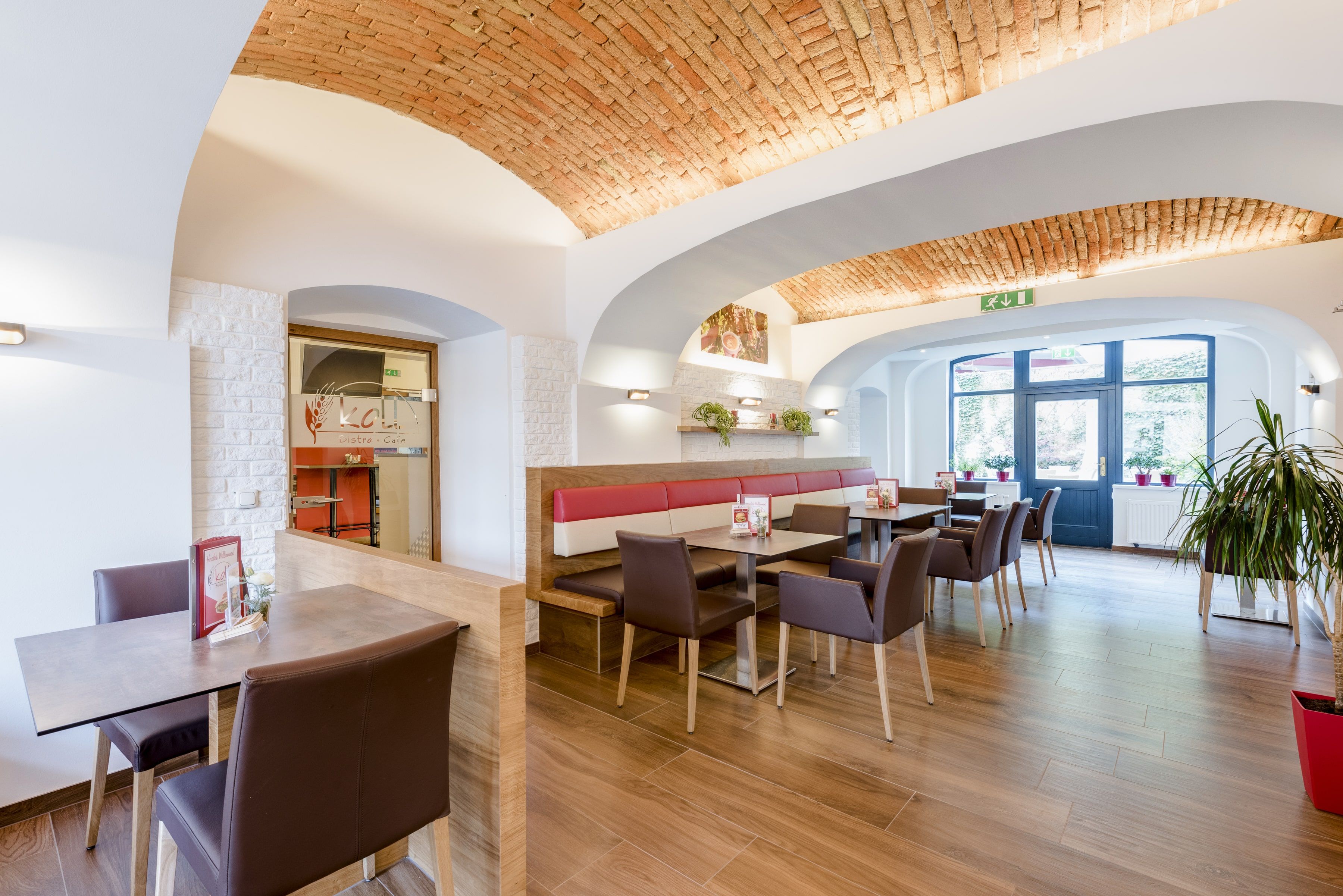 Innenansicht eines modernen Bistros mit gewölbter Ziegeldecke, Holzboden und stilvollen Sitzbereichen.