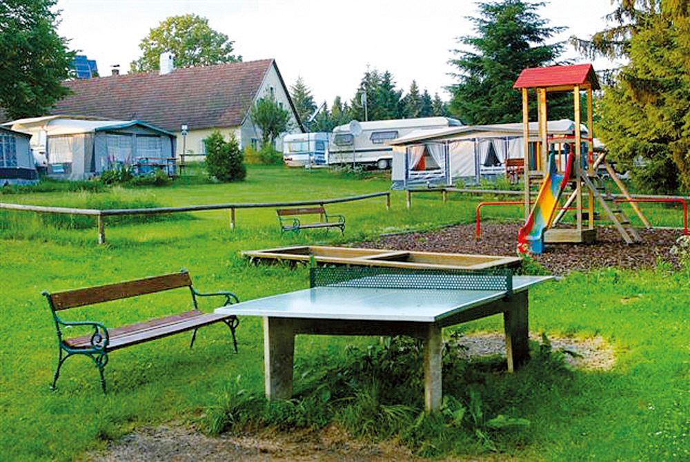 Campingplatz mit Tischtennisplatte, Spielplatz und Wohnwagen.