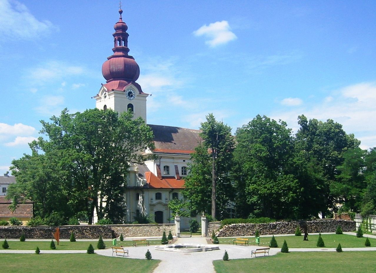Barockkirche mit rotem Turm und Garten im Vordergrund.