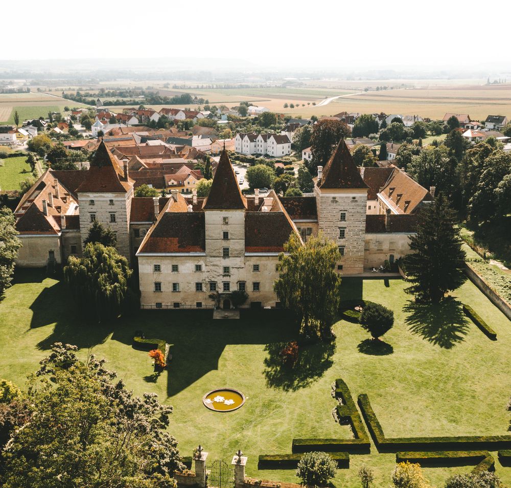 Eingang von Schloss Walpersdorf mit offenem Tor, Rasenfläche und historischem Gebäude im Hintergrund.
