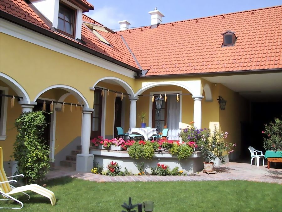 Gelbes Haus mit rotem Dach, Arkaden und Terrasse mit Blumen.